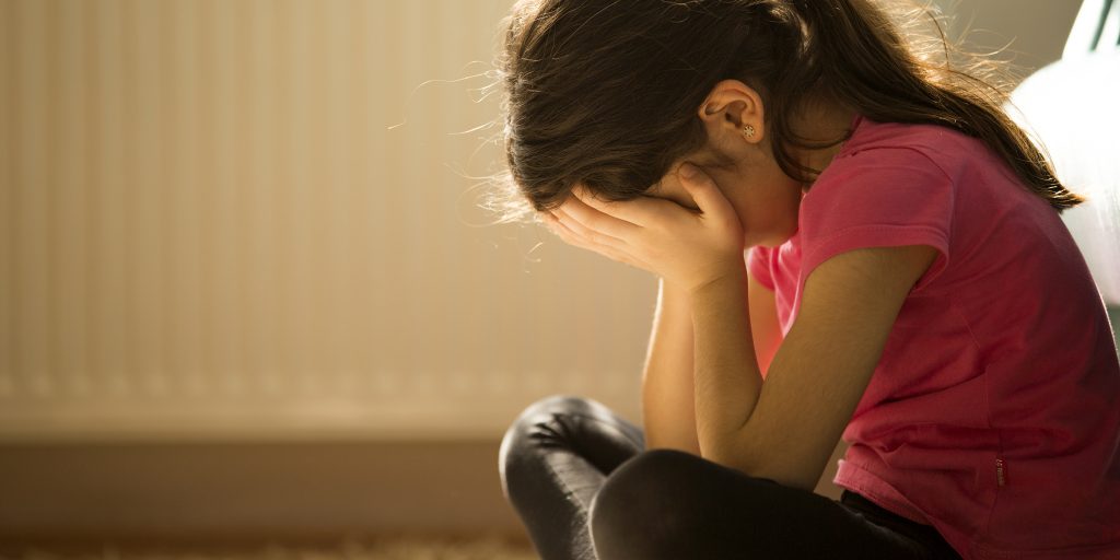 Image of young girl sitting with her legs tucked and her face in her hands.